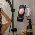 Luminomo Orbit magnetic phone mount attached to a shower wall holding a smartphone for hands-free music and media use in the bathroom.